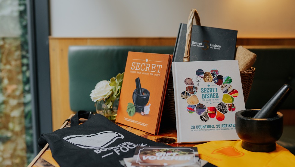 A selection of Bounceback Food merchandise arranged on a table including cookbooks, t-shirts, aprons and gift vouchers.