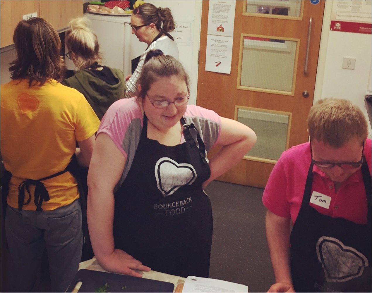 A Community Cookery School participant stands by a saucepan wearing an apron.